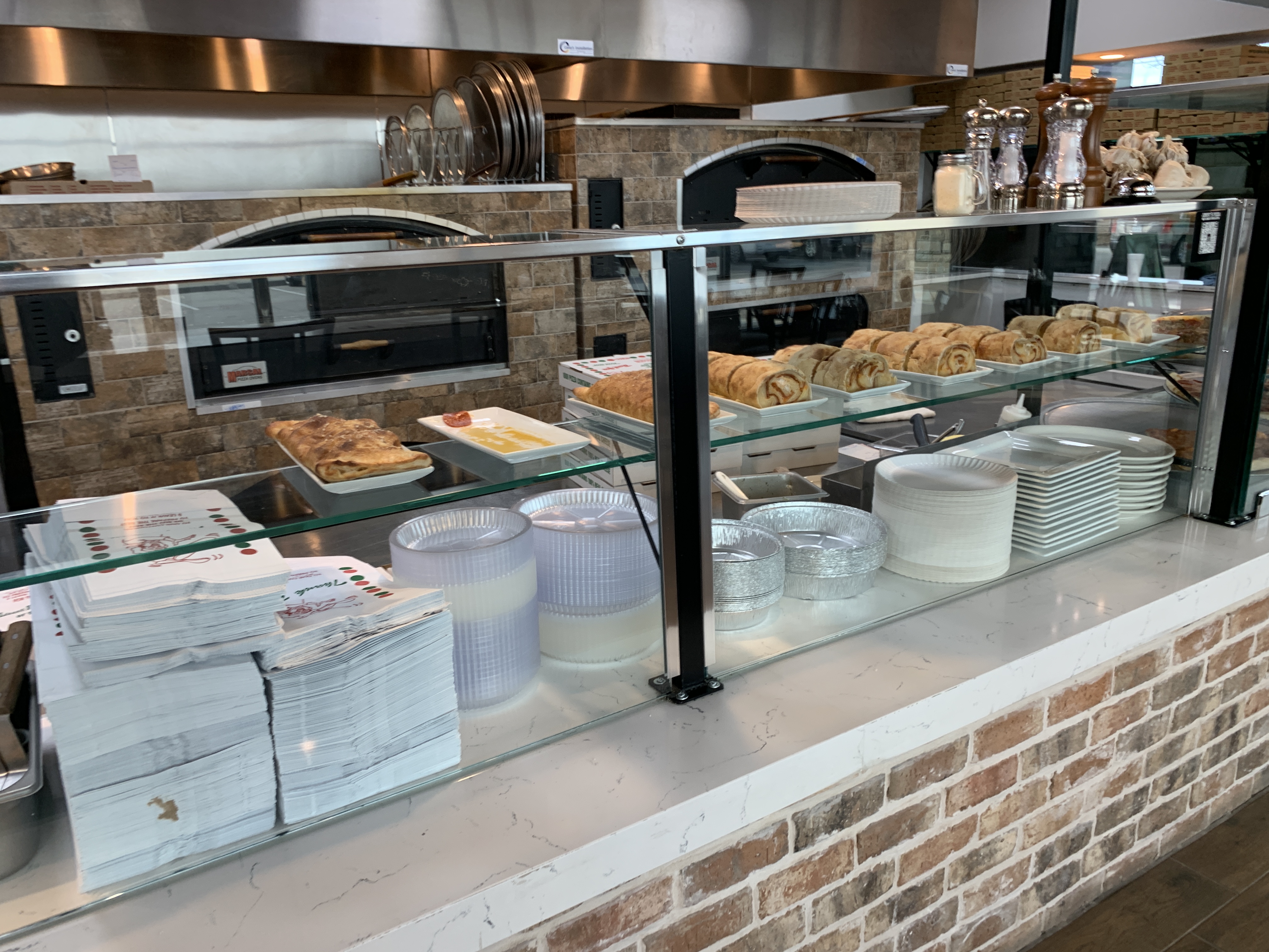Fresh-baked stromboli, cinnamon rolls, and to-go containers ready at the counter at Jonny's Pizza in Frisco, TX