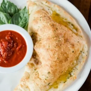 Hand-tossed New York-style calzone with fresh marinara dipping sauce and basil, made in house at Jonny's Pizza in Aubrey and Frisco, TX