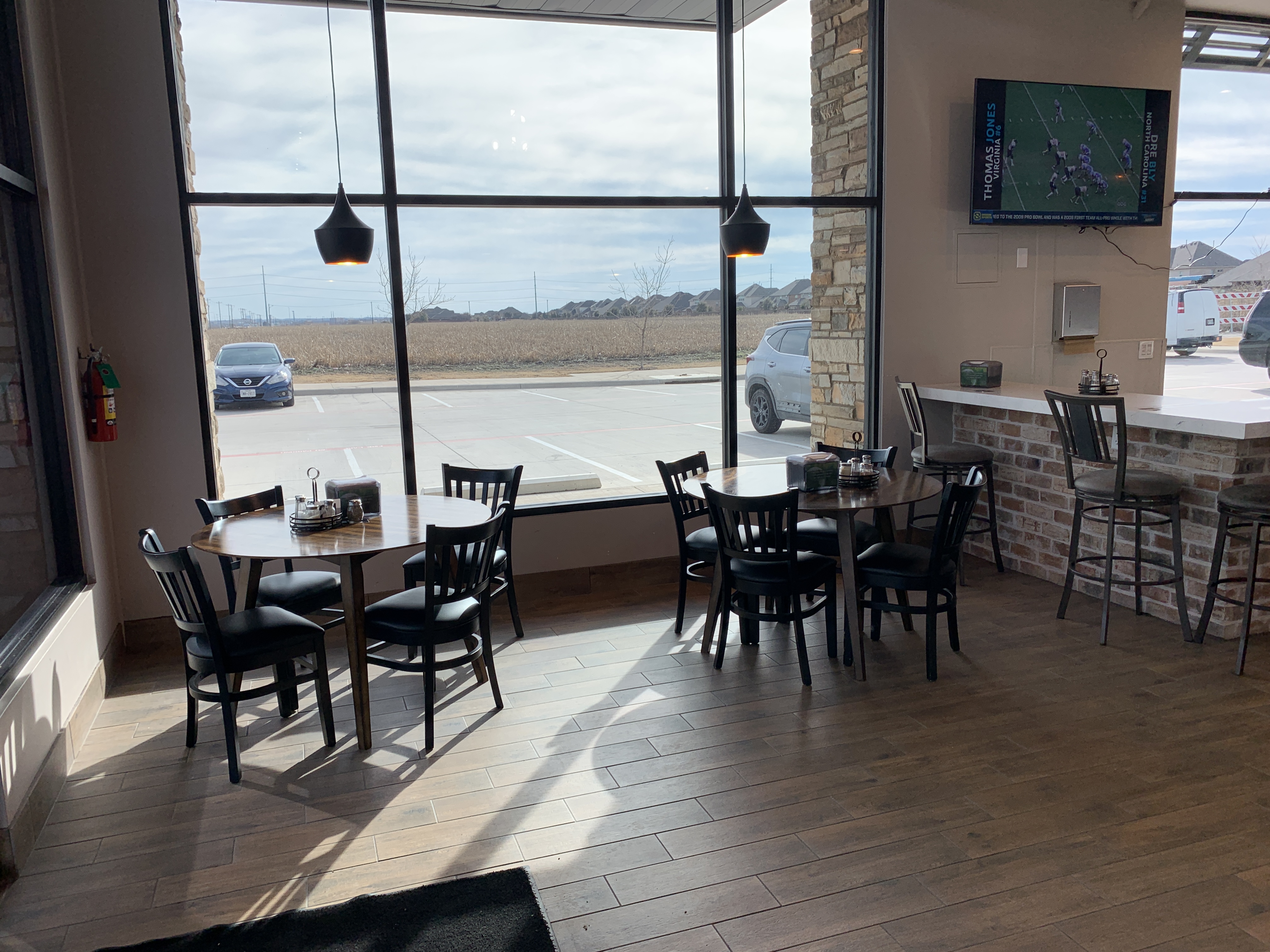 Dining tables near the window with a game on TV at Jonny's Pizza in Frisco, TX